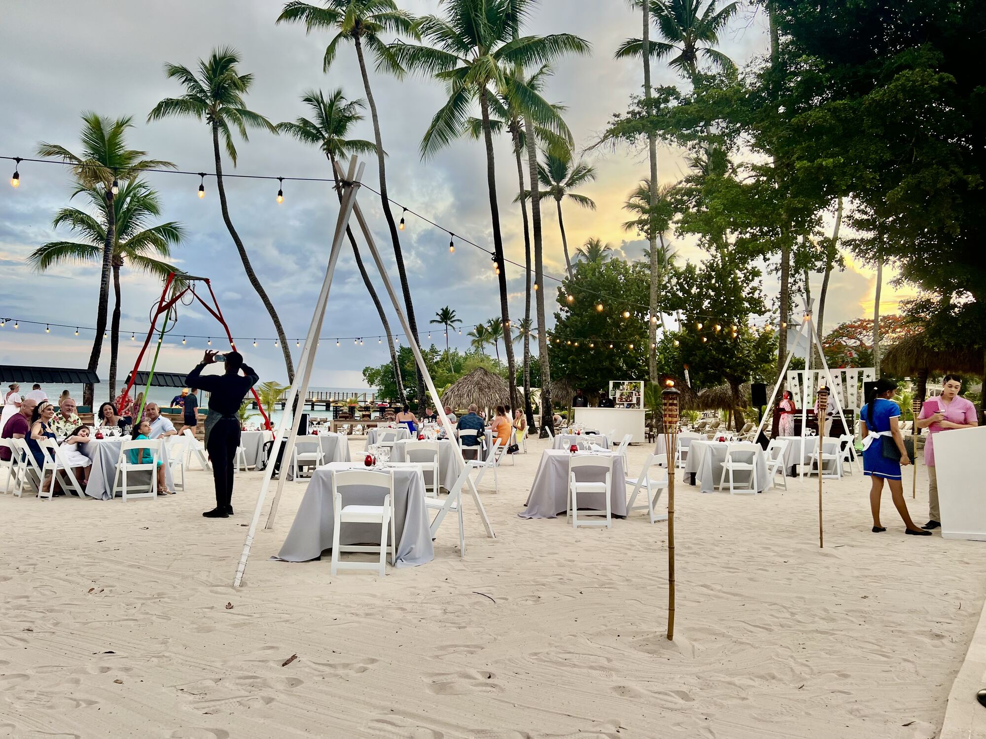 Friends gathered at a warmly-lit terrace dinner during a destination wedding week — the atmosphere guests are protecting on their calendars when a save-the-date arrives