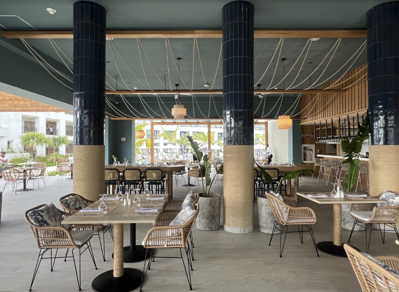 Seaside Grill Restaurant at Secrets Playa Esmeralda with woven chairs, black columns, and open-air dining space