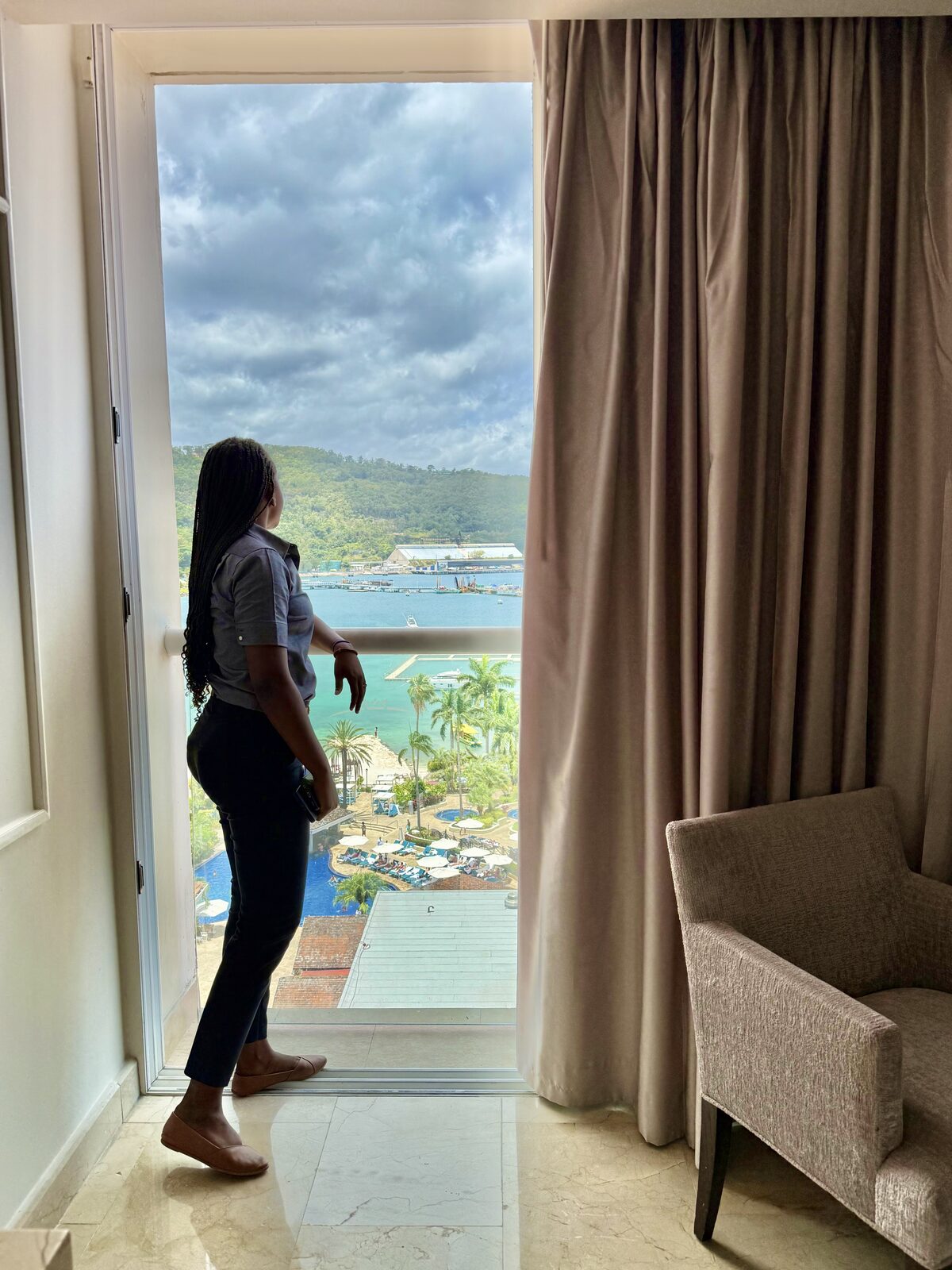 A woman on a resort balcony overlooking the pools, the kind of arrival window when the gown should be unpacked and hung so it can breathe before the wedding