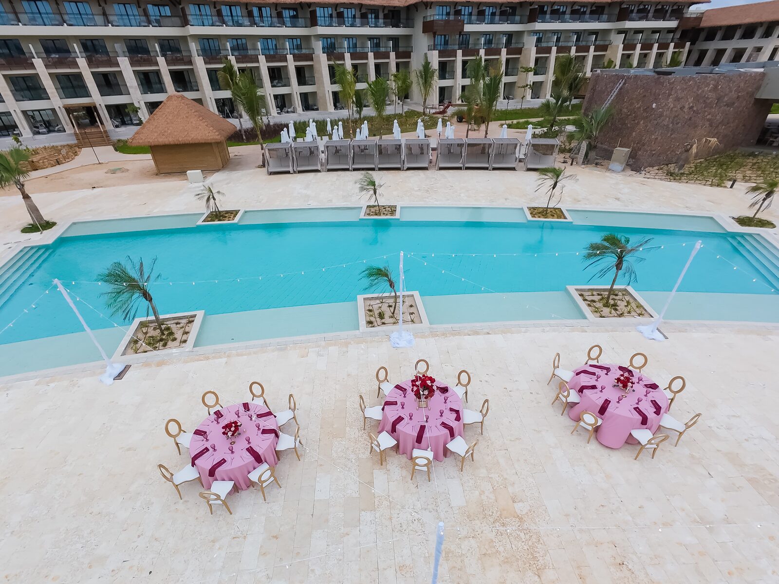 Dreams Playa Esmeralda pool terrace reception setup with pink round tables beside the pool and resort buildings