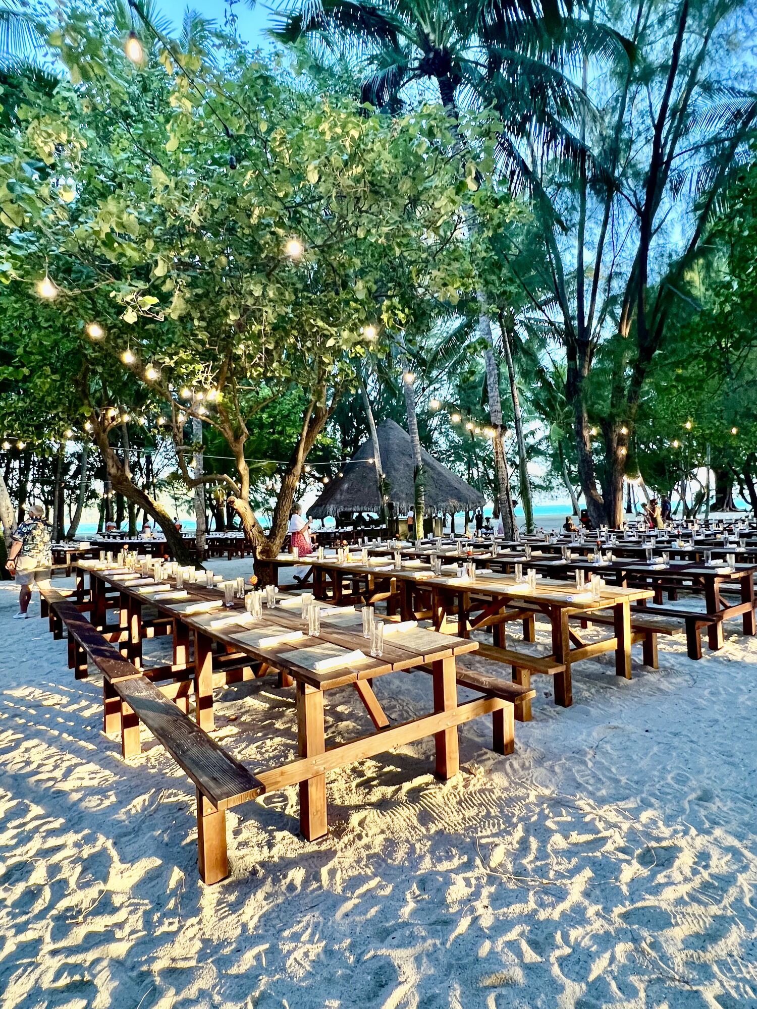 Beachfront reception setup at dusk with paper lanterns and burlap chair sashes — evening celebrations remain magical even outside peak dry season