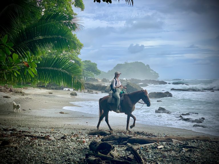 Guest horseback riding along a rocky tropical beach in Costa Rica near the Pacific Ocean