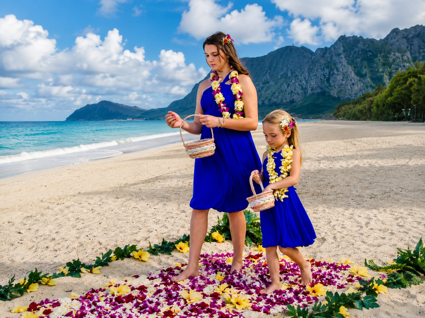 Two flower girls in royal blue dresses carrying baskets during a beach wedding ceremony in Oahu, Hawaii