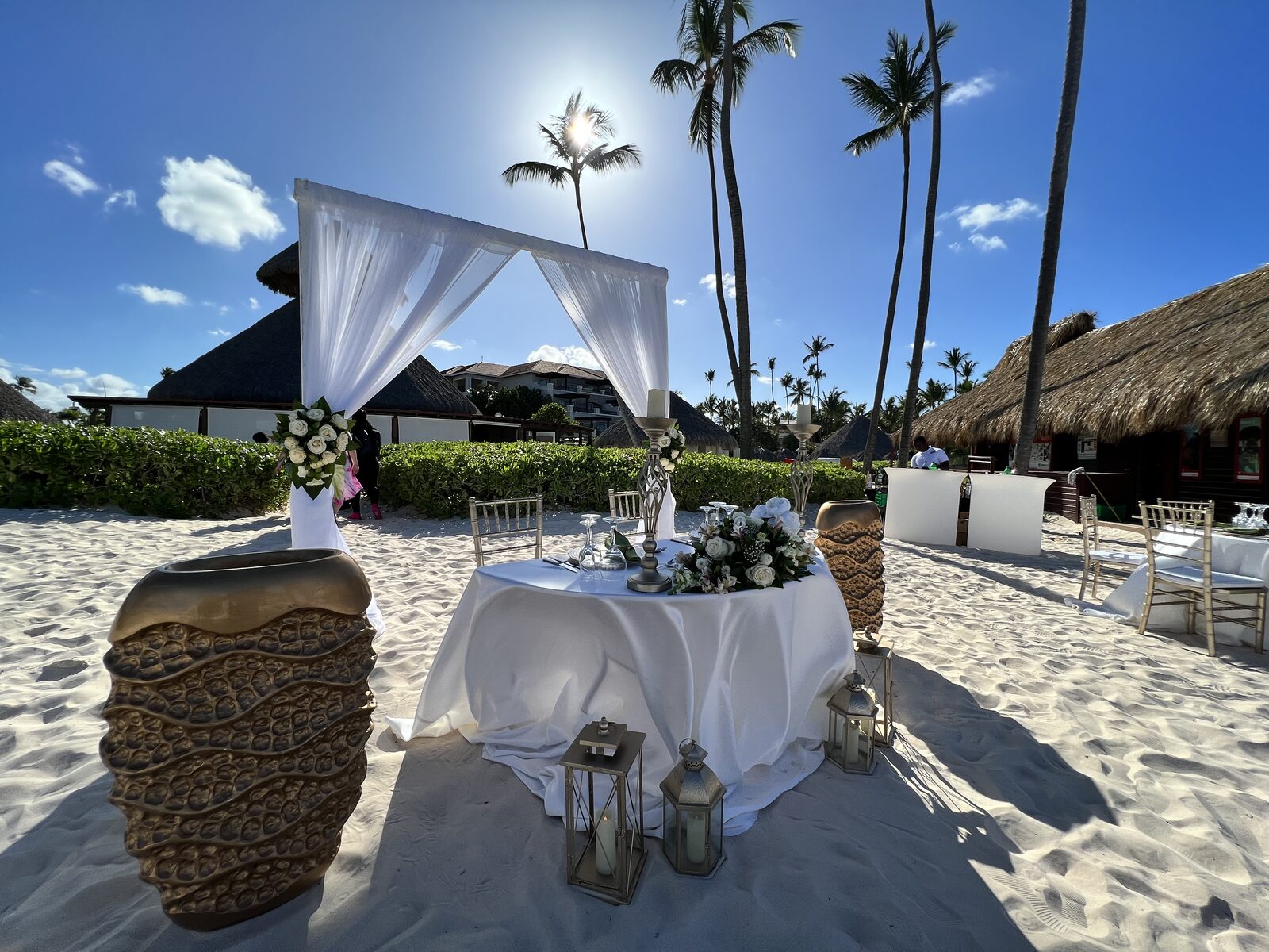 A beach sweetheart table lit with lanterns at dusk, the intimate anchor point of the reception where speeches land toward the couple and the room together
