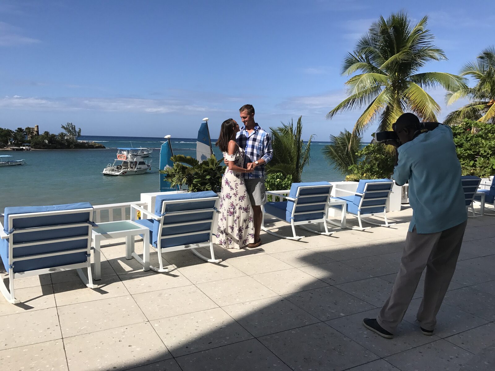 A photographer capturing a couple alone on a resort terrace with the ocean in the background — the exact kind of quiet, private moment couples are choosing to save their personal wedding vows for