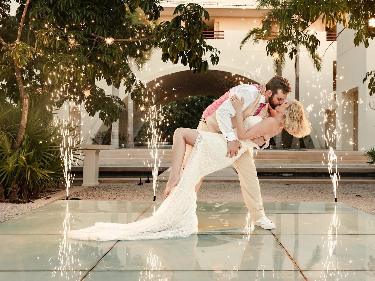 A bride and groom dip-kissing on an illuminated dance floor surrounded by sparkler fountains at their destination wedding reception