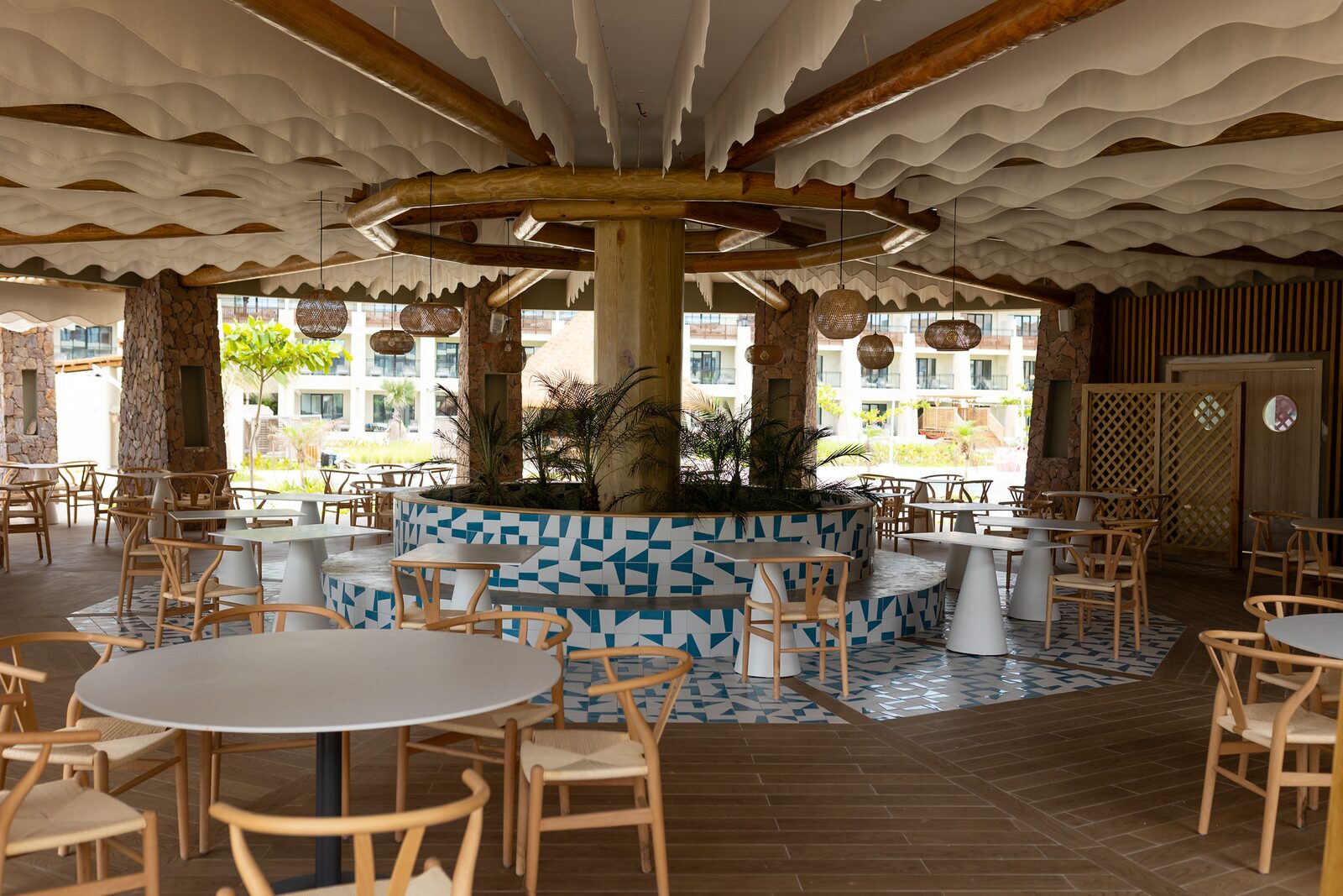Bluewater Restaurant at Dreams Playa Esmeralda with light wood chairs, blue tile details, and wave-shaped ceiling panels
