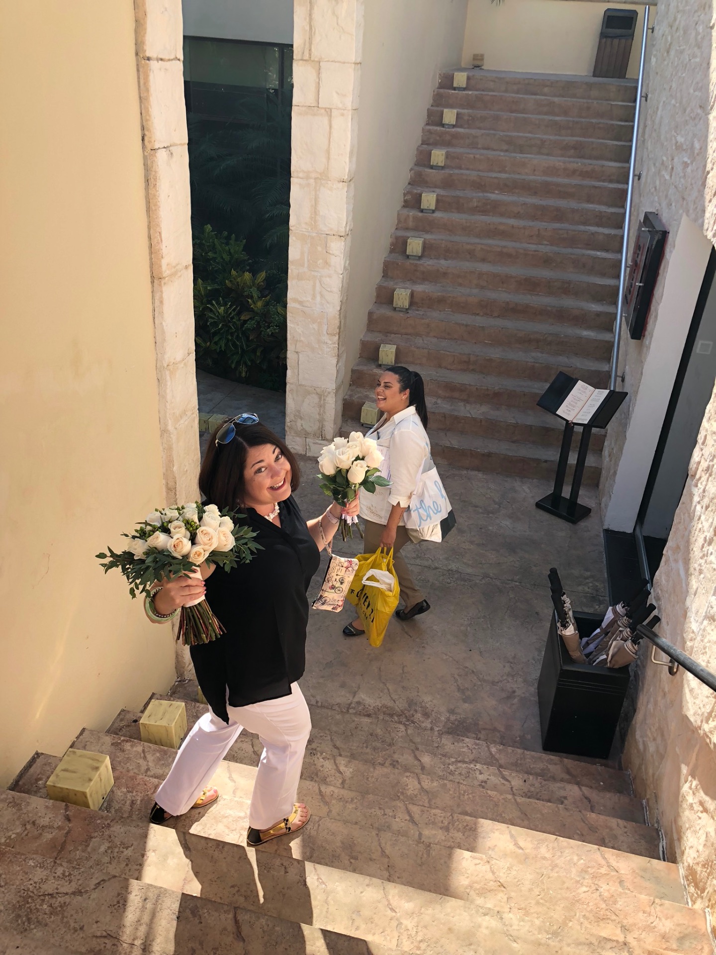 Shanna and a colleague carrying white rose bouquets down an outdoor staircase