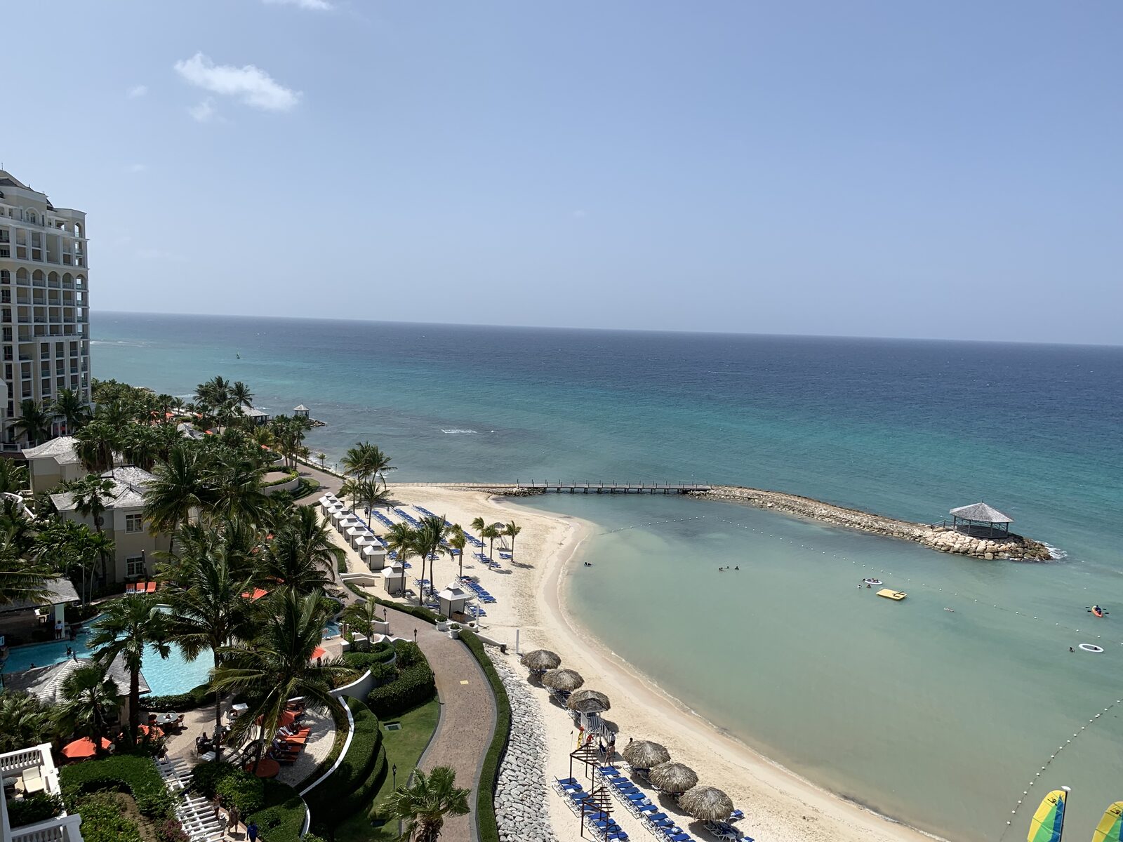 Aerial view of a resort beach cove with a wedding gazebo and pier extending into the water, the kind of dramatic Cabo-style setting that costs 10 to 20% more than a comparable Riviera Maya venue