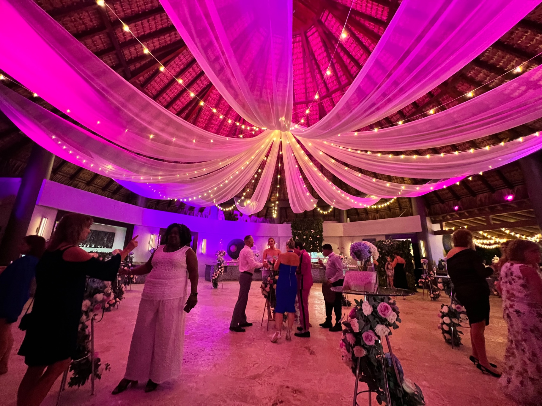 Guests mingling under string lights and colorful uplighting at a destination wedding welcome event