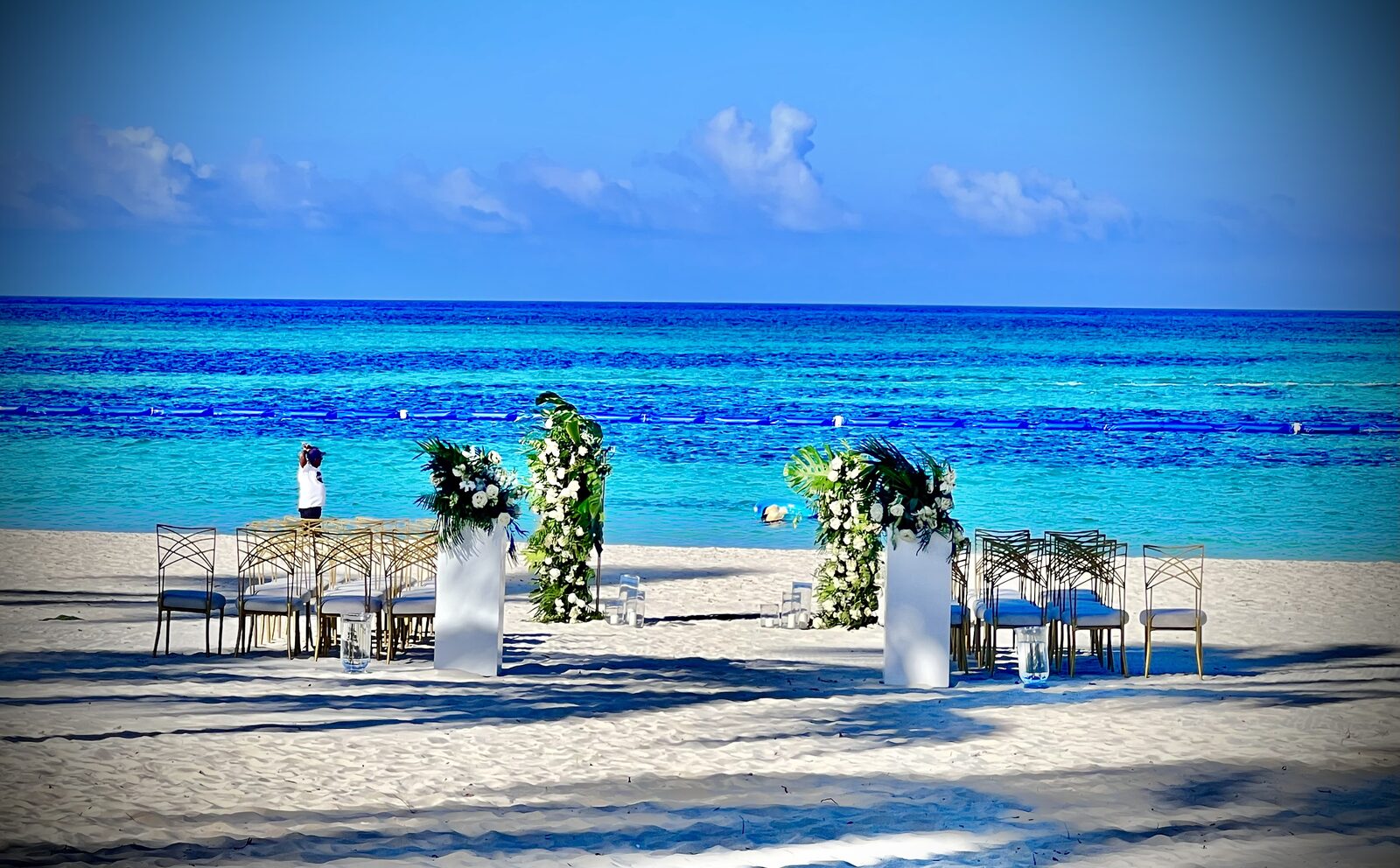 A beachfront ceremony setup with white pillars and florals waiting for guests, the kind of intimate setting where a family friend officiant works well