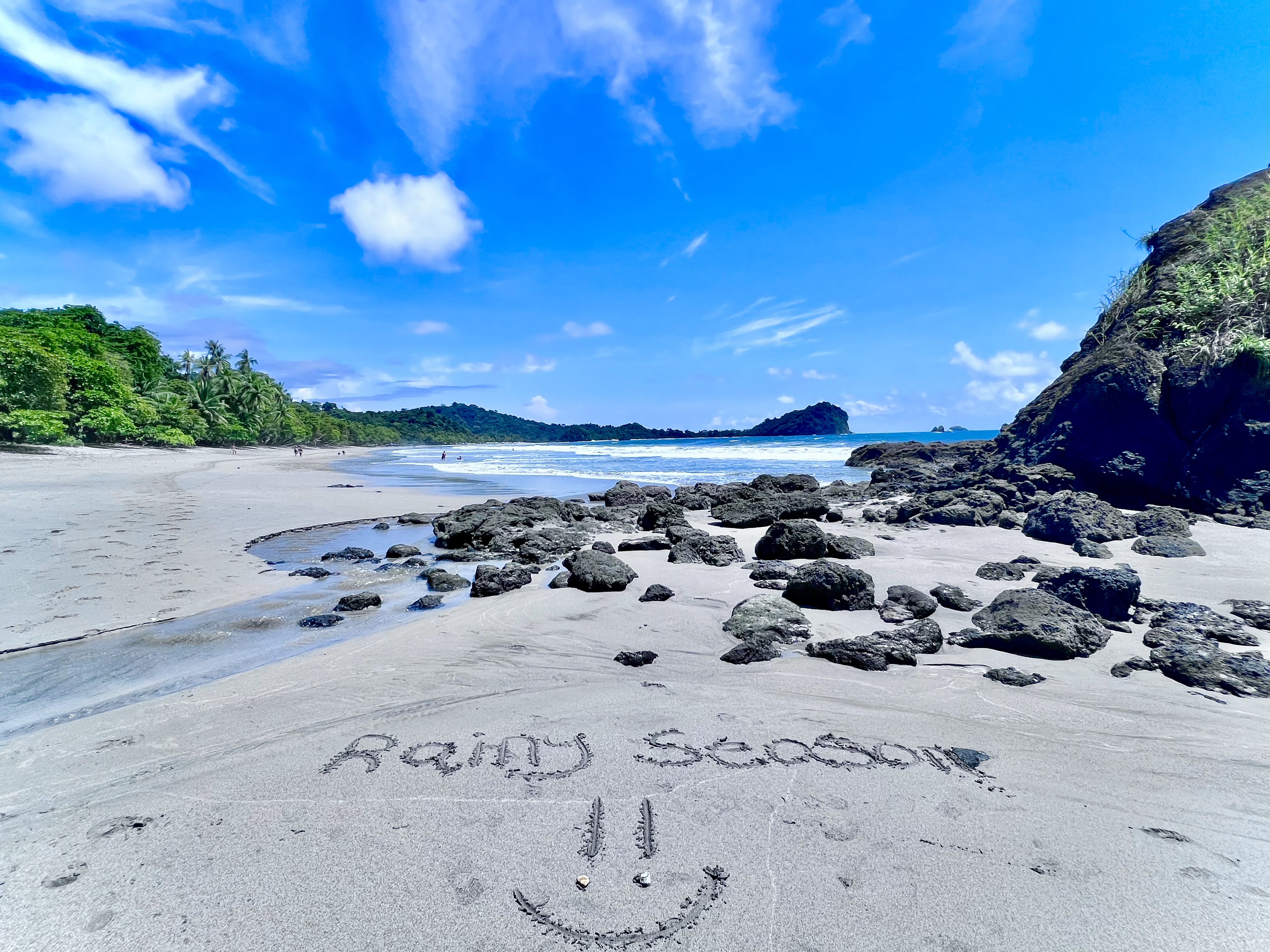 Green season morning in Manuel Antonio, Costa Rica, with sandy beach, volcanic rocks, and lush rainforest