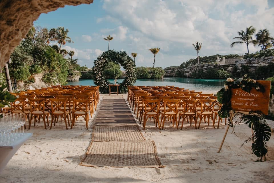 Xcaret beachfront ceremony setup with wooden chairs and a floral arch overlooking turquoise water