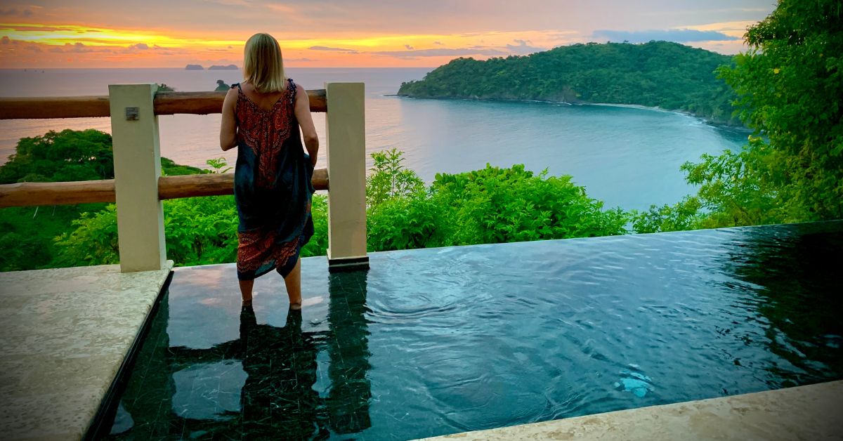 Woman standing in an infinity pool overlooking the Costa Rica coastline at sunset