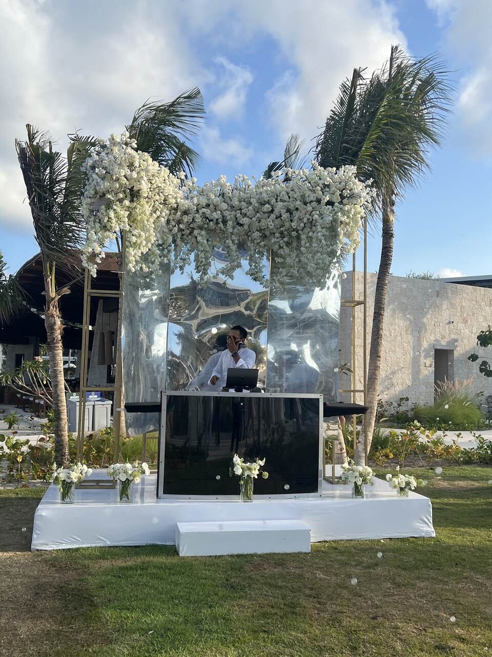 Wedding DJ booth decorated with white florals and mirrored panels at a beachfront destination wedding