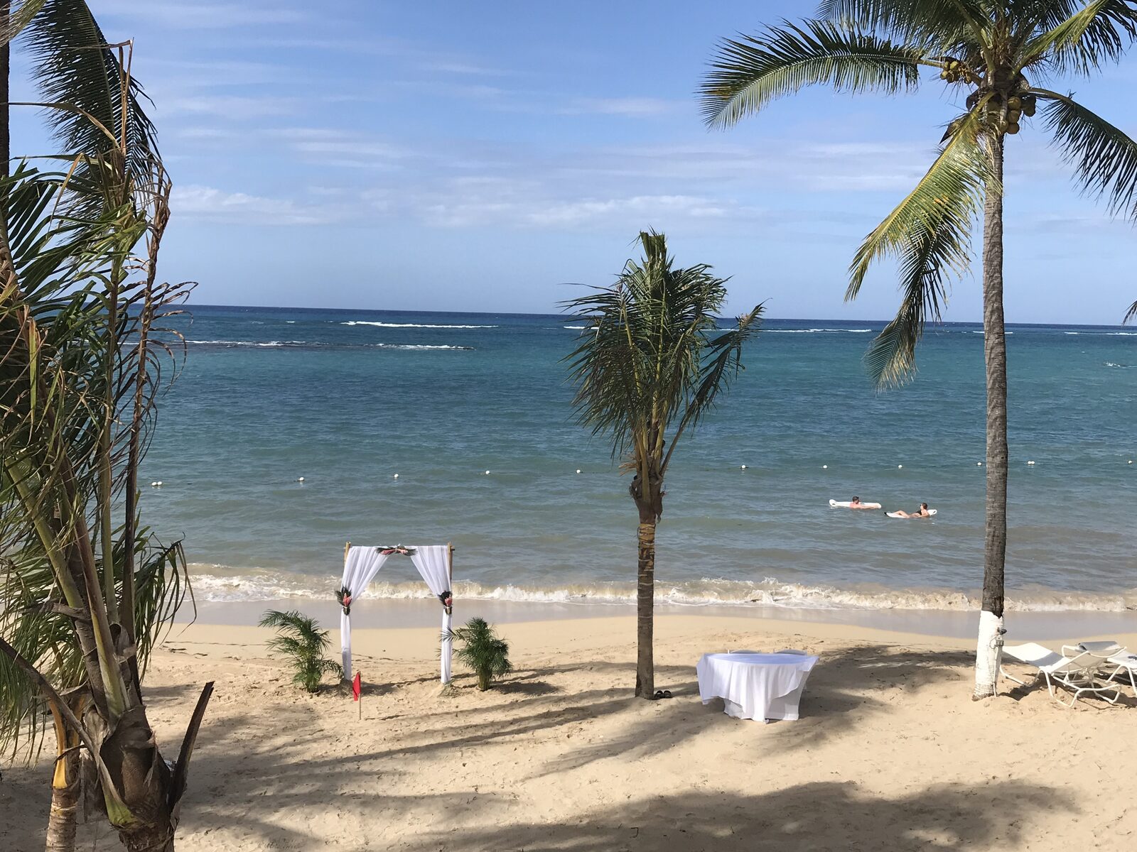 A white draped wedding arch on a Mexico beach with the ocean behind it, the kind of setup that shows up in couples' first Pinterest boards when they start thinking about a destination wedding