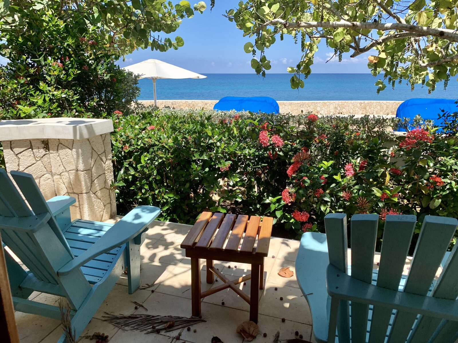 Two blue Adirondack chairs on a private resort patio overlooking the ocean, evoking the shared-room arrangement destination wedding guests often use to make the trip affordable