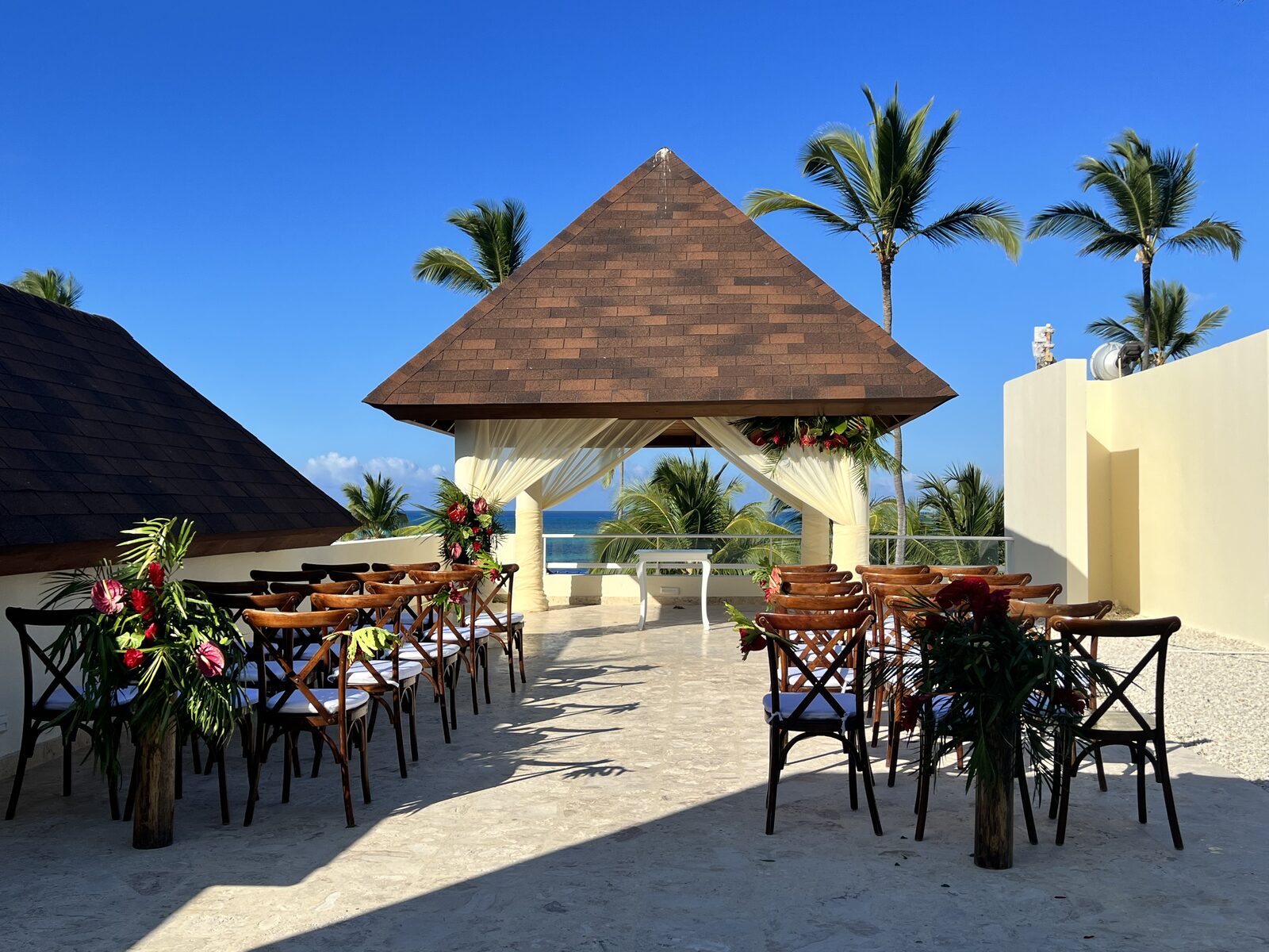 A rooftop pergola ceremony aisle overlooking the ocean, the kind of destination setup where the officiant needs a lapel mic and a printed script that survives the wind