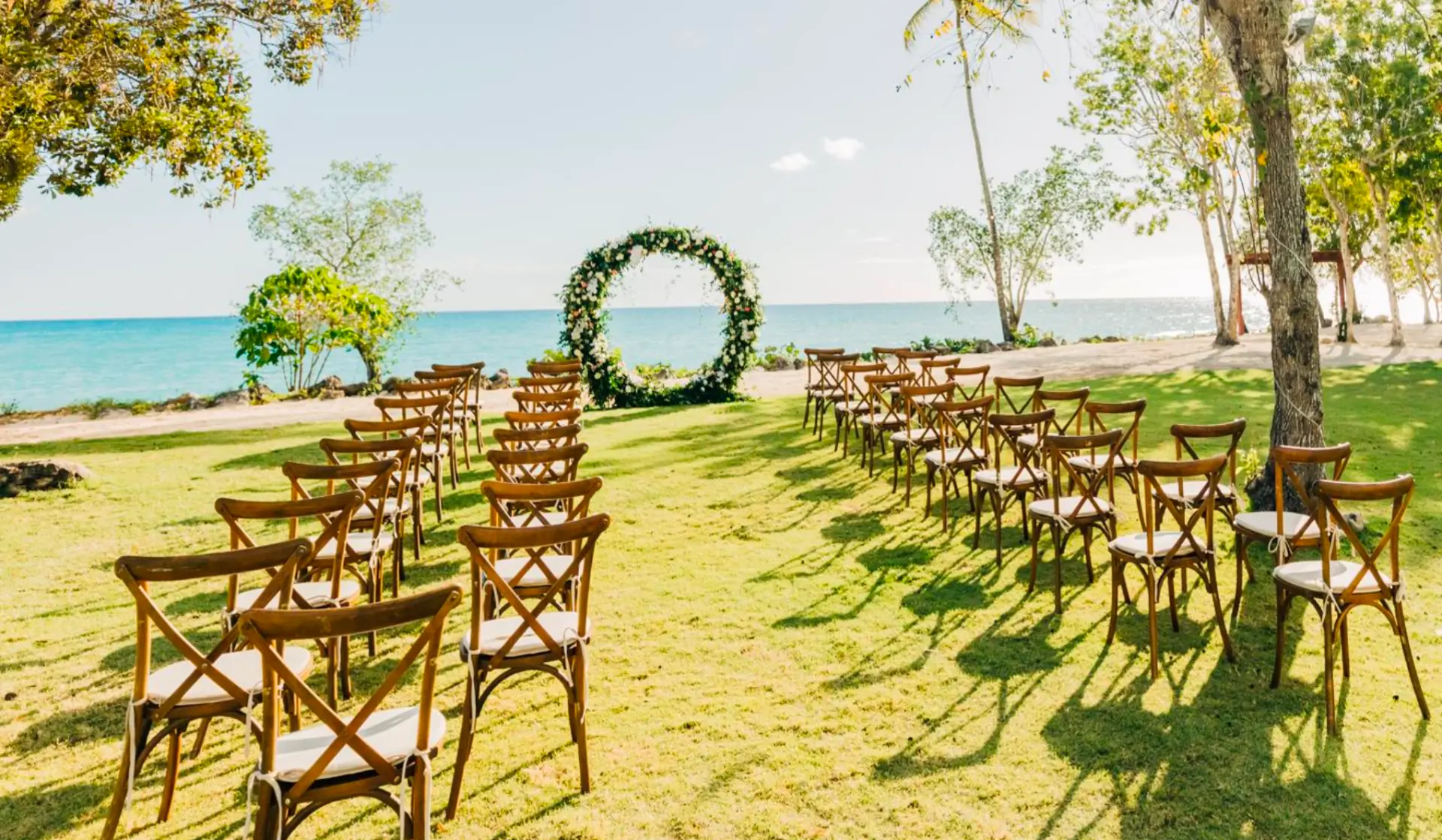 Circular floral wedding arch on the Sunset Garden lawn by the ocean, with rows of wooden chairs set for the ceremony