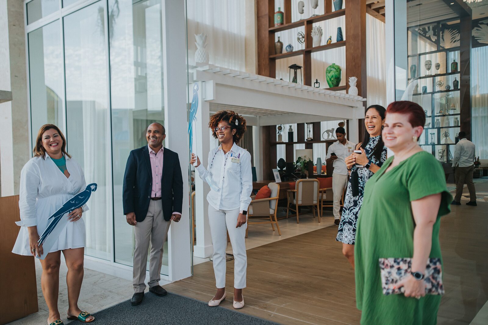 A resort staff member greeting an arriving group in a bright glass-walled lobby with a welcome sign — the moment a well-timed airport transfer is designed to deliver you into, instead of an hour of curbside waiting