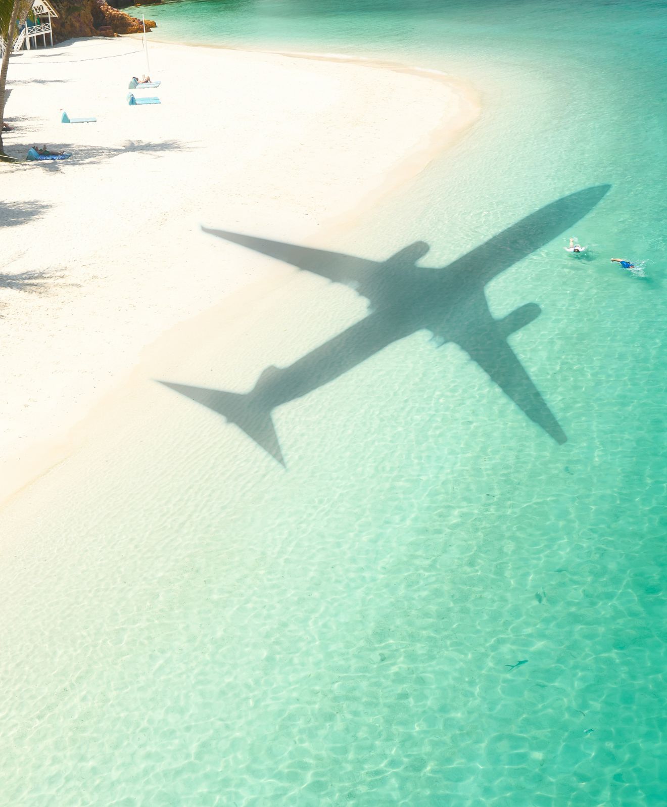 Shadow of an airplane cast over a curve of white sand beach and clear turquoise Caribbean water.