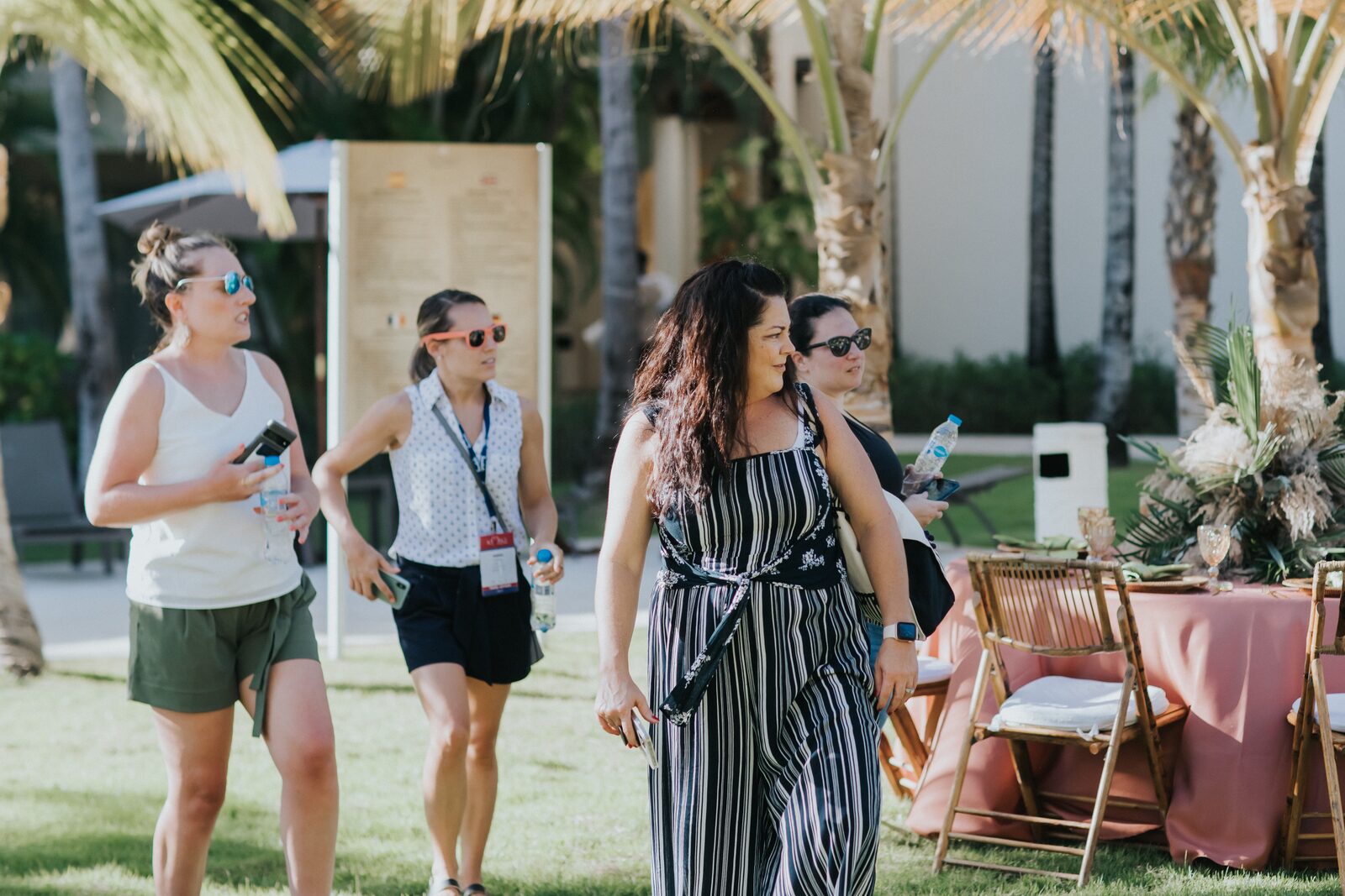 A group of women friends walking together across a resort event lawn on the way to a destination wedding welcome party, the kind of built-in travel buddies that come with a smart roommate arrangement