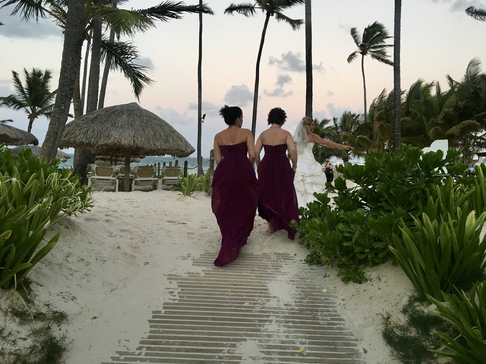 A bride and her bridesmaids walking down a resort beach path at sunset, the kind of built-in friend group that roommate arrangements are designed to keep affordable for everyone