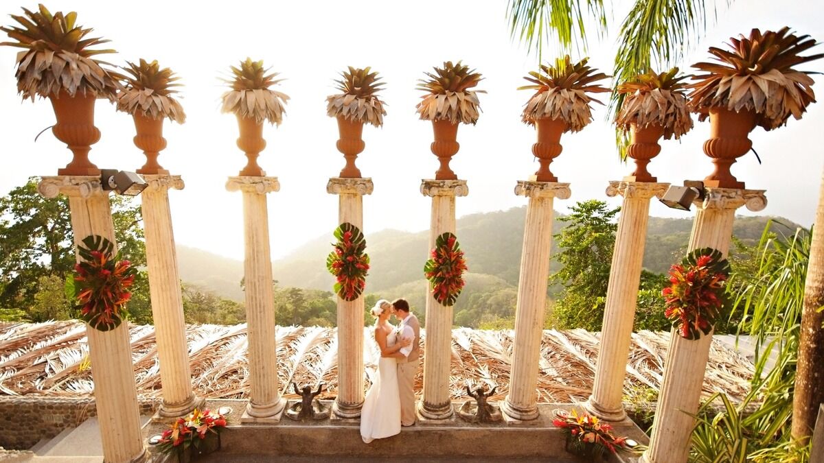 Couple embracing under a columned archway at golden hour with Costa Rica mountains in the background