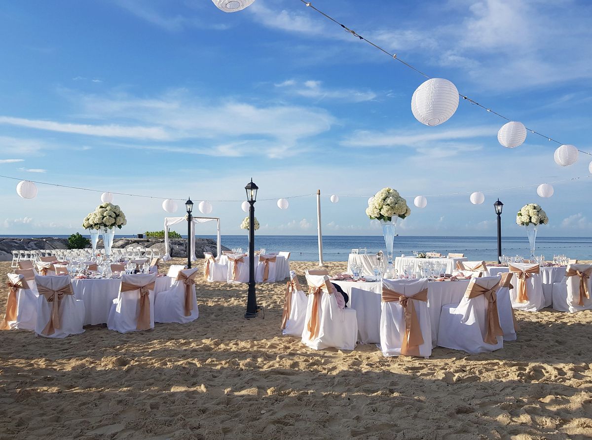 Beach reception setup with paper lanterns and rustic chair sashes for a destination wedding welcome event